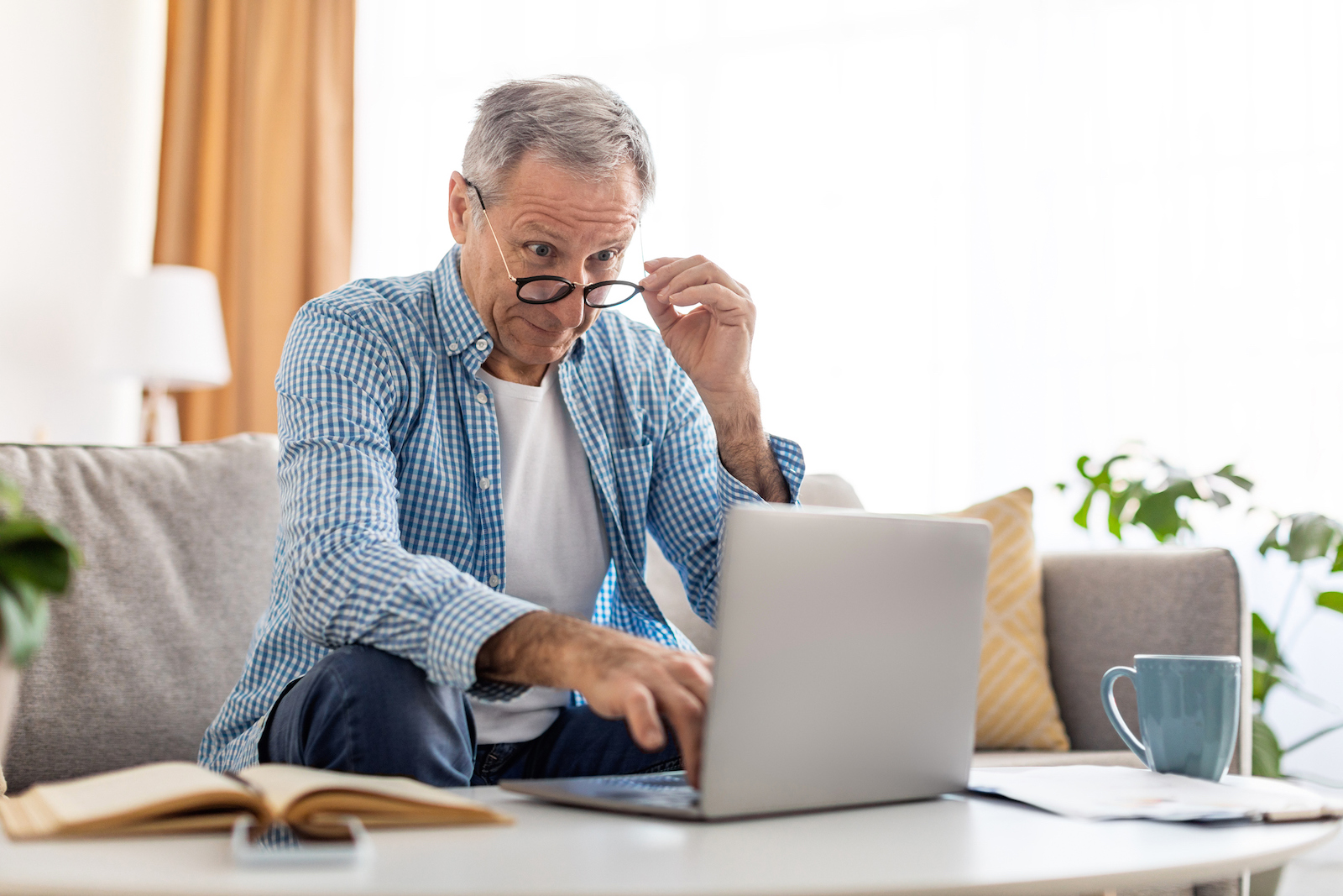 Mature man using laptop, taking off glasses, looking at screen.